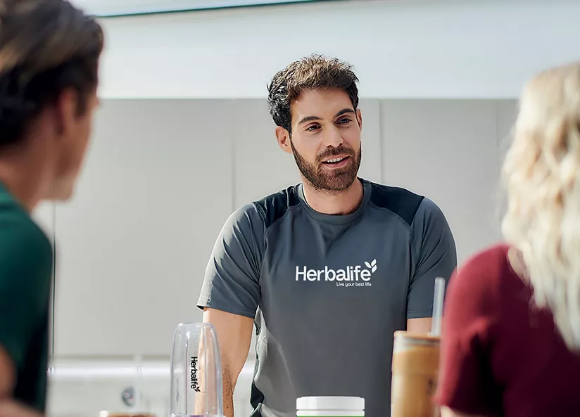 Coach de Herbalife explicando los beneficios de la nutrición a dos clientes.